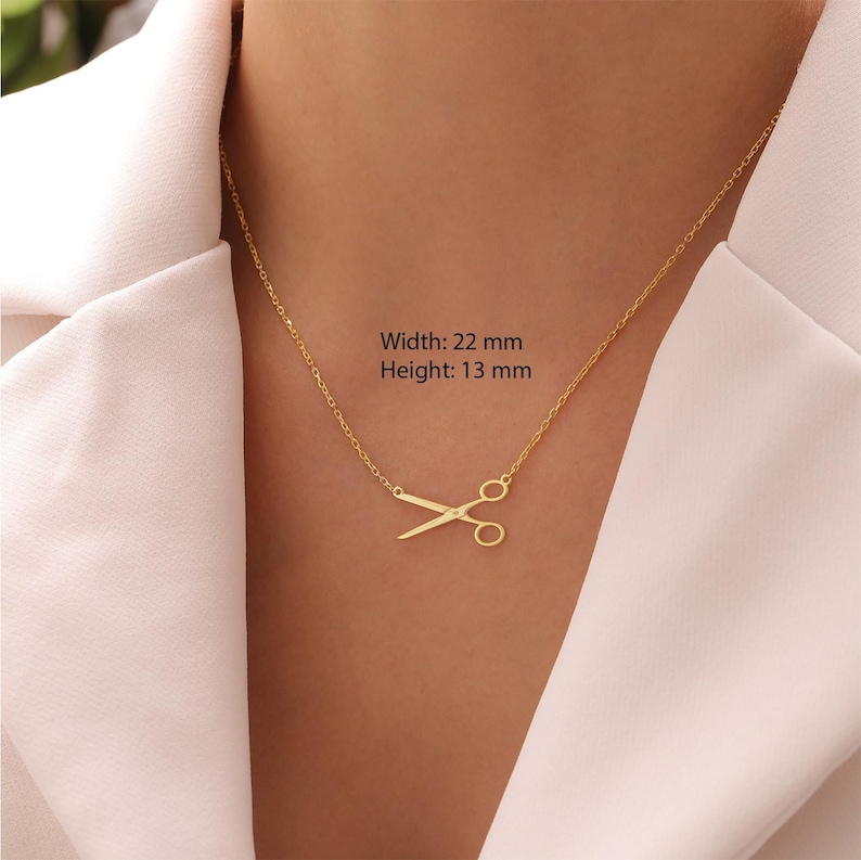 May include: A gold-coloured necklace with a scissors pendant. The scissors pendant is 22 mm wide and 13 mm high. The necklace is shown against a white background.