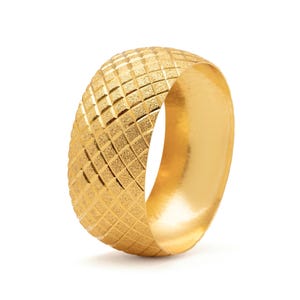 Puede incluir: Un anillo dorado con una superficie texturizada con patrón de diamantes. El anillo tiene un interior liso y pulido y una banda ancha. El anillo es una joya.