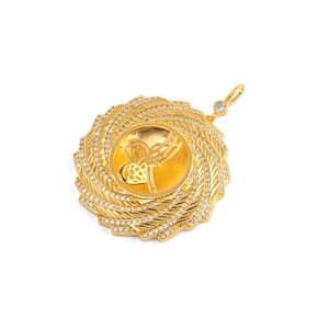 May include: A gold pendant with a circular design. The pendant features a central medallion with an ornate design, surrounded by a spiral of smaller, sparkling stones. A small loop with a single stone is at the top.