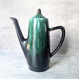 Peut inclure: Une cafetière en céramique haute avec une anse et un bec noirs. Le pot est verni dans des tons de vert et de noir, avec un effet dégoulinant. Le couvercle est vert assorti. Un article de cuisine vintage.