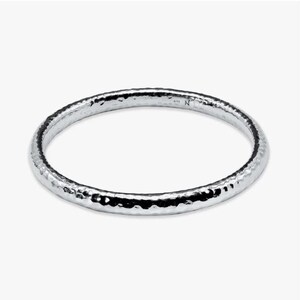 May include: A silver bangle bracelet with a hammered texture. The bracelet is a simple, circular design, and the metal has a shiny, reflective quality. The bracelet is a classic piece of jewellery.