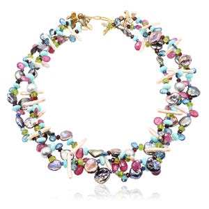 May include: A colorful necklace featuring a variety of gemstones and pearls. The necklace includes pink, blue, green, and iridescent stones, along with white, oblong pearls. The necklace is strung on a gold-colored chain.