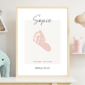 May include: A framed print with a pink baby footprint, the name "Sophie", and the birth date and time. The print also shows the baby's weight, 3500 g, and height, 51 cm. The frame is light-coloured.
