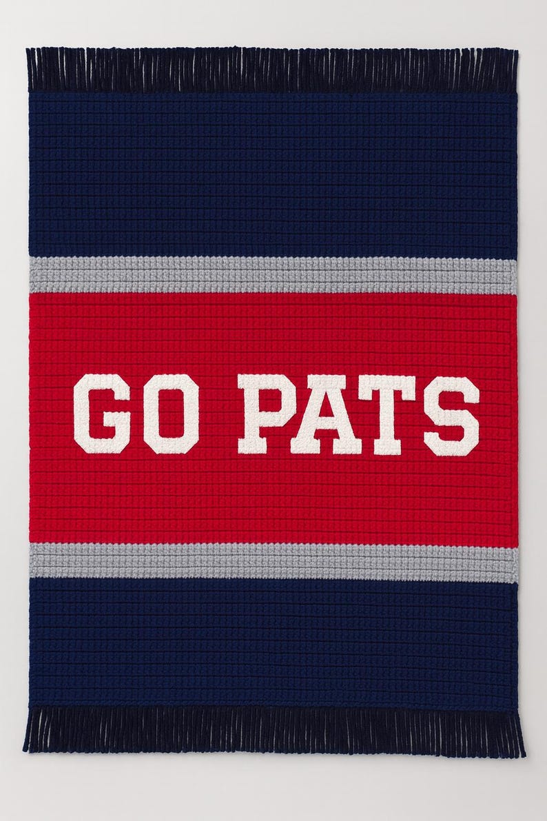 May include: A rectangular, knitted blanket in navy blue, red, and gray, with a fringe along the bottom edge. The words "GO PATS" are displayed in large, white, block letters across the center red stripe.