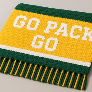 May include: A handmade, crocheted scarf in green, yellow, and white, with the words "GO PACK GO" in bold white letters. The scarf has a fringed edge with yellow and green tassels, perfect for showing team spirit.