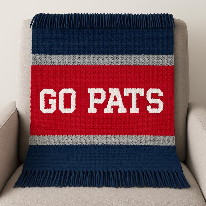 May include: A crocheted blanket in navy blue, red, and gray, with the words "GO PATS" in white block letters. The blanket has a fringed edge and is draped over a chair. The design is a tribute to a sports team.
