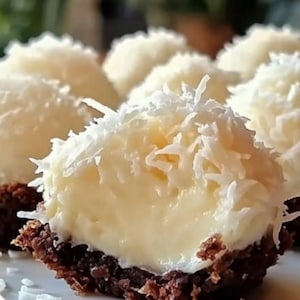 Puede incluir: Primer plano de varios postres de crema de coco. Cada postre tiene una base marrón oscuro y desmenuzable, un relleno cremoso amarillo y está cubierto con coco rallado blanco. Los postres están dispuestos muy juntos.