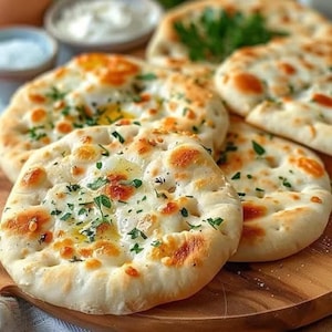 Peut inclure: Gros plan sur plusieurs pains plats ronds dorés, garnis de fromage fondu et d'herbes vertes hachées. Les pains plats sont disposés sur une planche de bois, avec un arrière-plan flou de petits bols.