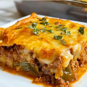 Peut inclure: Une portion de lasagnes sur une assiette blanche. Le plat est composé de couches de pâtes, de sauce à la viande, de poivrons verts et de fromage fondu, garni d'herbes fraîches. Le dessus des lasagnes est doré et croustillant.