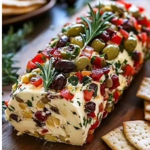 May include: A rectangular cheese log topped with olives, diced red tomatoes, and fresh rosemary sprigs. The log is surrounded by crackers on a wooden board, creating a visually appealing appetizer.