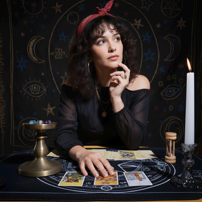 Puede incluir: Una mujer con una diadema roja y un top negro con hombros descubiertos est&aacute; sentada en una mesa con cartas del tarot. Una vela encendida, un reloj de arena y un cuenco de lat&oacute;n con dados tambi&eacute;n est&aacute;n sobre la mesa. El fondo es un tapiz negro con s&iacute;mbolos celestiales.