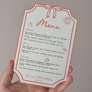 May include: A white menu card with a scalloped edge and a red border featuring a bow at the top. The text reads Menu, Starters, Mains, Desserts, and Louise's 35th birthday 29.07.2027. It includes illustrations of champagne glasses, a disco ball, and cake.