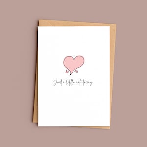 May include: A white card with a pink heart design and the handwritten text "Just a little note to say..." sits on a brown envelope. The background is a solid mauve colour.