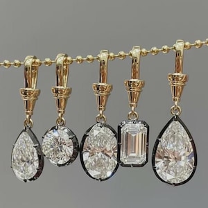 May include: Five gold earrings with different diamond shapes: pear, round, oval, emerald, and pear. Each diamond is set in a dark metal bezel and hangs from a gold chain.