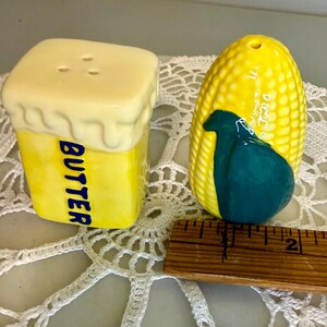 May include: A pair of ceramic salt and pepper shakers. One is shaped like a yellow butter stick with the word "BUTTER" in blue. The other is a yellow corn cob with a teal design.
