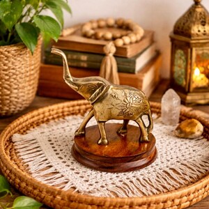 May include: A golden brass elephant figurine on a wooden base, displayed on a woven tray with a white lace doily. The elephant has detailed floral patterns and is part of a home decor theme.