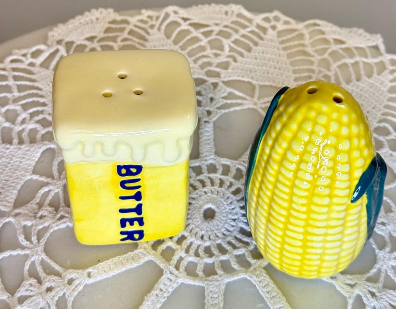 May include: A pair of ceramic salt and pepper shakers. One is shaped like a stick of butter with the word "BUTTER" in blue. The other is shaped like an ear of corn with yellow kernels and green and blue husks.