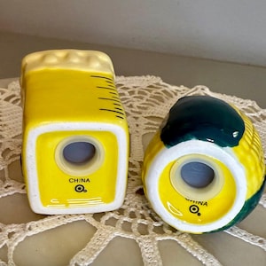 May include: A pair of ceramic salt and pepper shakers. One is shaped like a beer mug, yellow with a white foam top and black lines. The other is a yellow corn cob with green ends. Both have a hole for dispensing and the text "CHINA".