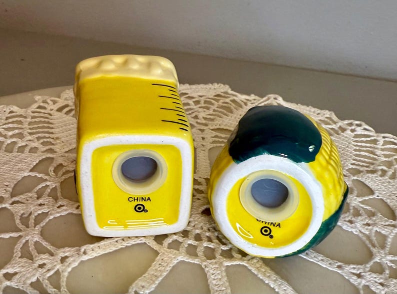 May include: A pair of ceramic salt and pepper shakers. One is shaped like a beer mug, yellow with a white foam top and black lines. The other is a yellow corn cob with green ends. Both have a hole for dispensing and the text "CHINA".