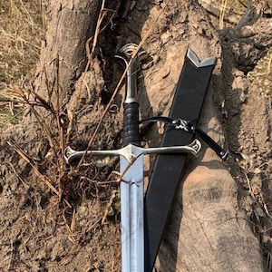 May include: A silver and black sword with a cross-shaped hilt and a leather sheath. The sword is leaning against a weathered tree trunk, with the blade partially drawn. The handle is black, and the blade is silver.