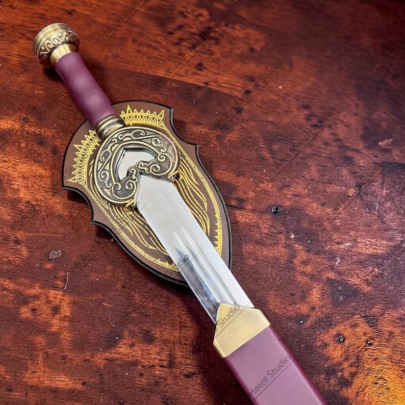 May include: A decorative sword with a purple handle and a gold-colored hilt. The sword features a silver blade and is mounted on a wooden shield with gold-colored accents. The sword is approximately 18 inches long.