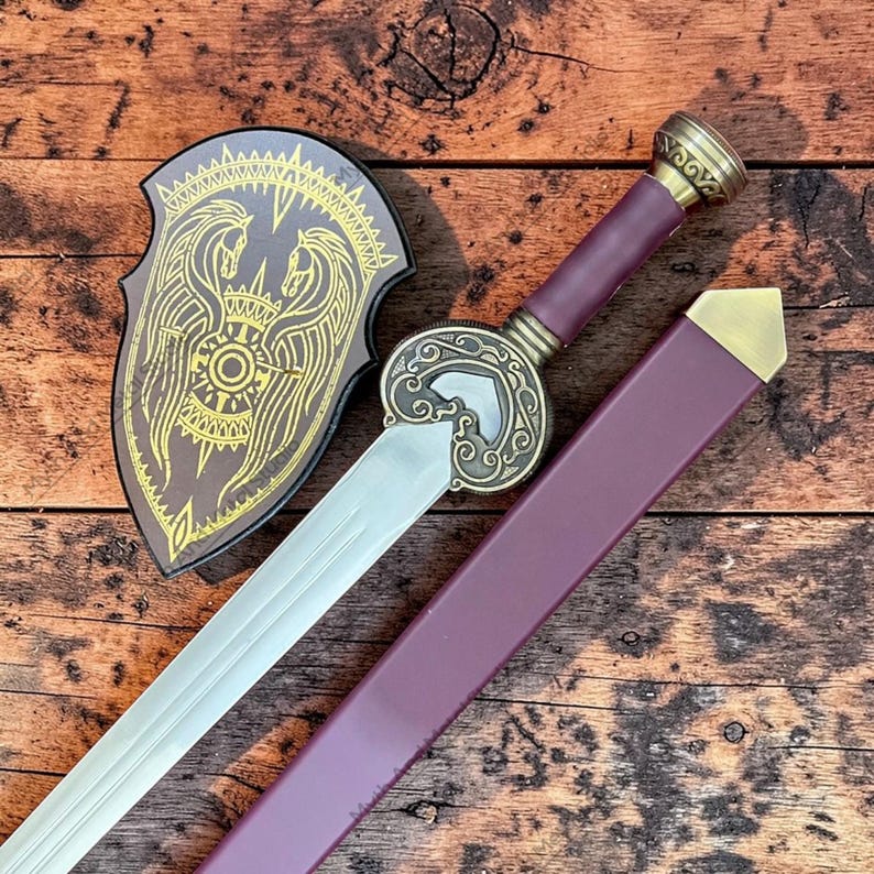 May include: A decorative sword with a silver blade, burgundy handle, and gold accents. The sword is paired with a matching burgundy sheath and a shield featuring a gold emblem of two horses. The shield is brown with gold trim.