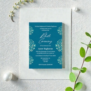 May include: A teal invitation card for a Dhot Ceremony, with ornate floral designs. The card includes the names Krishna Raghavan and Pramita Raghavan, and the name Aarav Raghavan. The invitation is on a white background with floral accents.