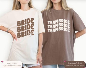 Puede incluir: Dos mujeres con camisetas, una marfil y otra espresso. La camiseta marfil tiene la palabra "BRIDE" repetida tres veces en marrón, con un gráfico de anillo. La camiseta espresso tiene "TEAMBRIDE" repetido tres veces en blanco, también con un gráfico de anillo. Ambas son informales y holgadas.