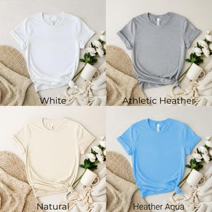K&ouml;nnte beinhalten: Vier unifarbene T-Shirts in verschiedenen Farben werden gezeigt. Die Farben sind Wei&szlig;, Athletic Heather, Natur und Heather Aqua. Jedes Hemd ist unten geknotet. Der Text "White", "Athletic Heather", "Natural" und "Heather Aqua" befindet sich darunter.