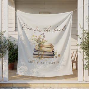 Könnte beinhalten: Cremefarbenes Banner mit dem Text "One for the books" und "LOLA'S 1ST CHAPTER". Das Banner zeigt eine Aquarellillustration eines Bücherstapels mit Blumen und einem Band. Das Banner hängt im Freien.