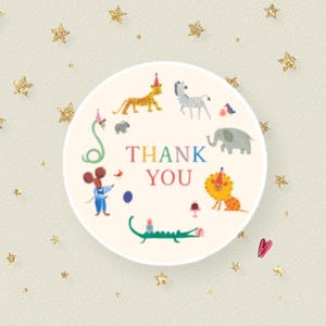 May include: A round sticker with the words "THANK YOU" surrounded by cartoon animals, including a lion, zebra, and elephant. The sticker has a cream background with gold stars.
