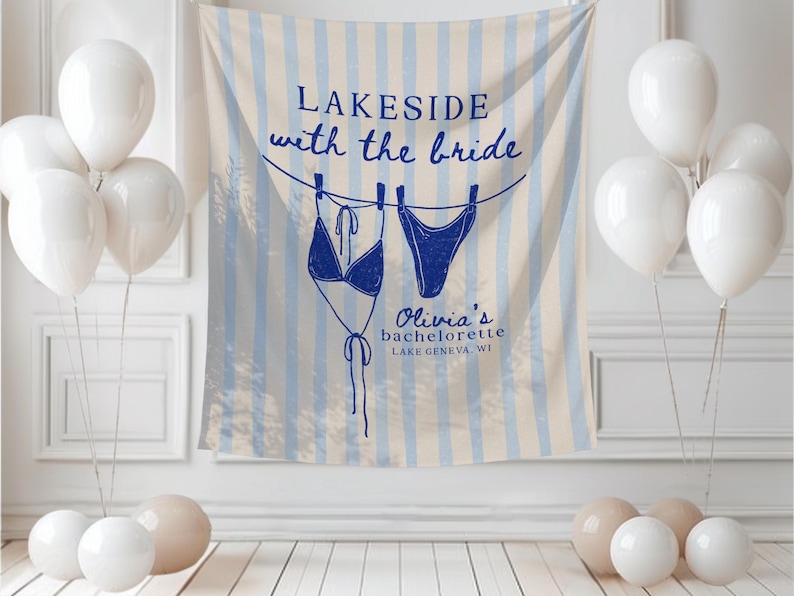 May include: A bachelorette party backdrop with blue and white striped design, featuring a drawing of a bikini. The text reads "Lakeside with the bride" and "Olivia's bachelorette Lake Geneva WI". White balloons and decorative spheres are in the foreground.