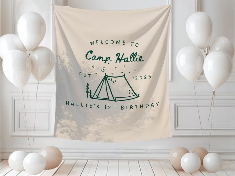 May include: A beige banner with the text "WELCOME TO Camp Hallie EST - 2025 HALLIE'S 1ST BIRTHDAY" in dark green. The banner features a tent illustration. White balloons are arranged around the banner, creating a festive atmosphere.