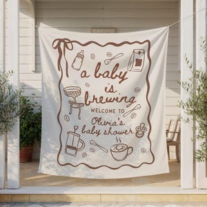 May include: A cream-colored banner with brown illustrations and text. The banner reads "a baby is brewing" and welcomes guests to Olivia's baby shower. The design includes coffee-themed drawings like a coffee cup, spoon, and coffee beans.
