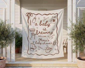 Puede incluir: Una pancarta color crema con ilustraciones y texto en marrón. La pancarta dice "a baby is brewing" y da la bienvenida a los invitados al baby shower de Olivia. El diseño incluye dibujos con temática de café.