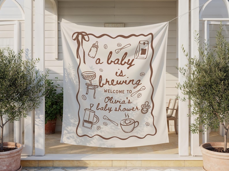 May include: A cream-colored banner with brown illustrations and text. The banner reads "a baby is brewing" and welcomes guests to Olivia's baby shower. The design includes coffee-themed drawings like a coffee cup, spoon, and coffee beans.
