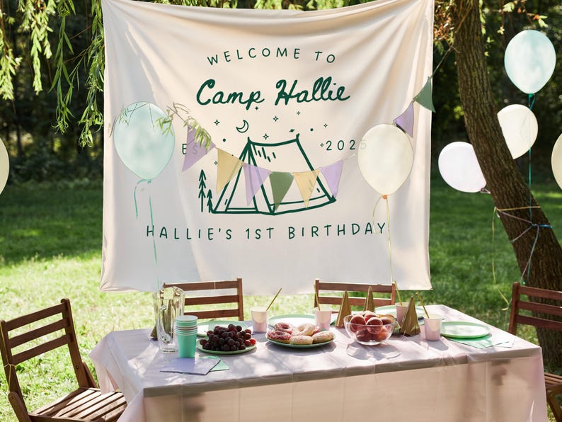 May include: A festive outdoor birthday party scene. A banner reads "Welcome to Camp Hallie" with a tent illustration and "Hallie's 1st Birthday". Balloons and a table set with food and drinks complete the celebration.