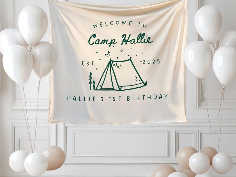May include: A cream-colored banner with the text "WELCOME TO Camp Hallie" and "HALLIE'S 1ST BIRTHDAY" in green. A green tent graphic is centered on the banner. White and tan balloons are arranged around the banner.