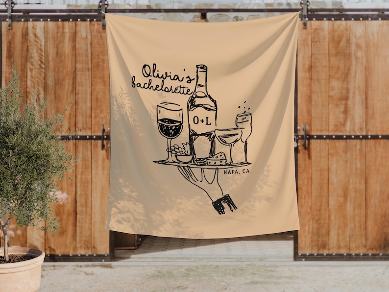 K&ouml;nnte beinhalten: Beige Stoffbanner mit einer schwarzen Illustration einer Weinflasche, Gl&auml;sern und Essen auf einem Tablett, gehalten von einer Hand. Der Text lautet "Olivia's bachelorette" und "NAPA, CA".