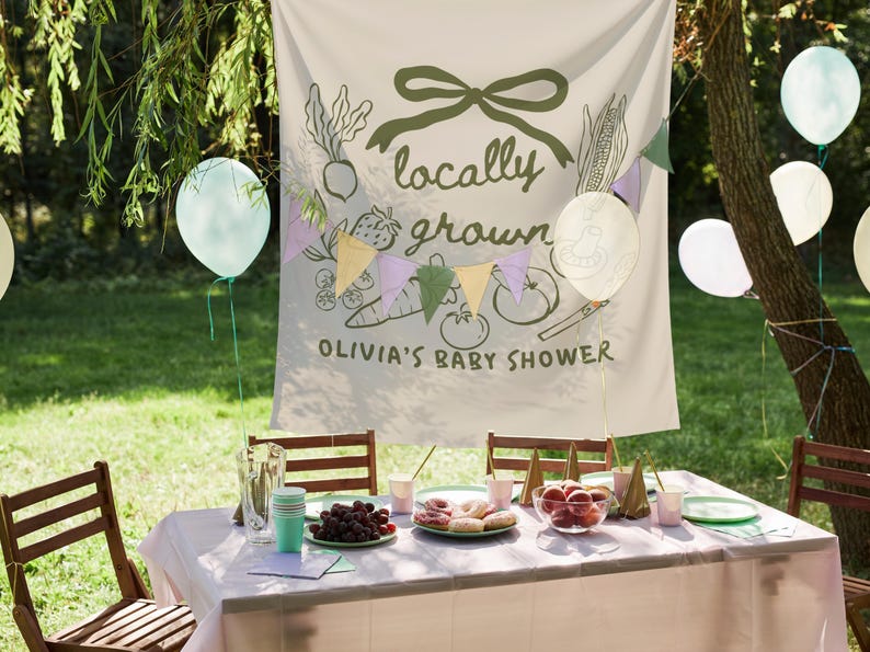 Może przedstawiać: Scena baby shower na świeżym powietrzu ze stołem przygotowanym na przyjęcie. Banner głosi "locally grown" z ilustracjami warzyw. Balony i girlandy zdobią scenę. St&oacute;ł jest zastawiony jedzeniem i napojami.
