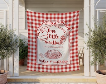 May include: A red and white checkered fabric banner with a white center panel. The panel features a chef's hat, fork, and text that reads "Our little meatball is turning one!" and "Milo's 1st birthday."