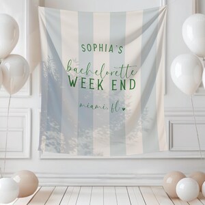 May include: A white and blue striped backdrop with the text "SOPHIA'S bachelorette WEEK END miami. fl." is surrounded by white balloons and beige and white orbs. The backdrop is hanging on a white wall.