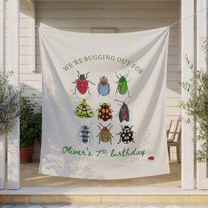 Peut inclure: Une bannière en tissu blanc présentant une grille de neuf illustrations d'insectes colorés. Le texte "WE'RE BUGGING OUT FOR" figure en haut et "Oliver's 7th birthday" en bas en écriture verte, avec une petite coccinelle près du texte.
