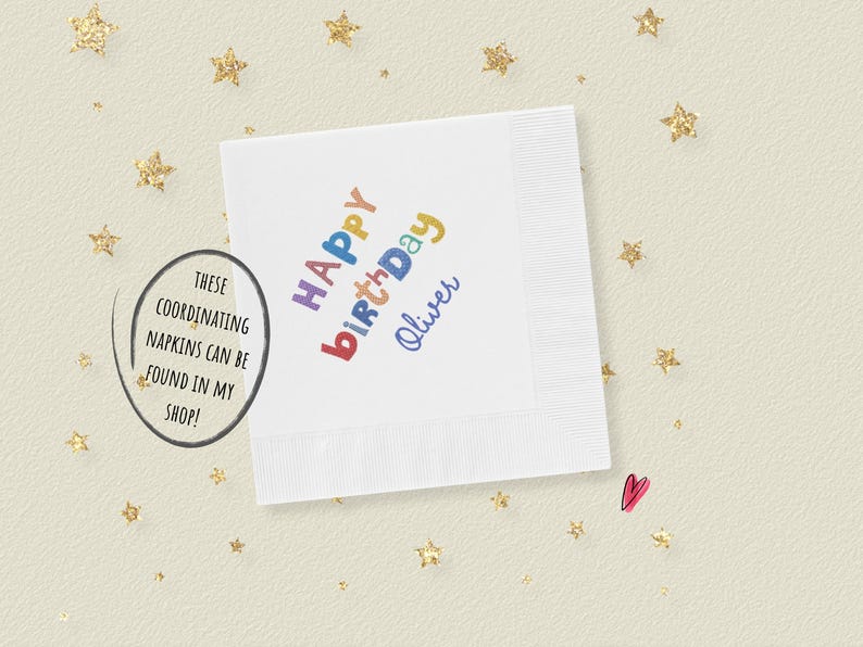 May include: A square white paper napkin featuring the text Happy Birthday Oliver printed in a multi-colored, playful font. The napkin is surrounded by scattered gold glitter stars and a small pink heart icon on a light cream-colored background.