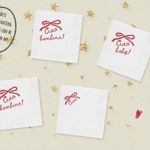 May include: White square napkins with a red bow and the words "Ciao bambina!" and "Ciao baby!" printed on them. The napkins are scattered on a cream-colored surface with gold star-shaped confetti.