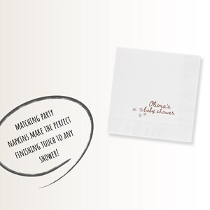 May include: White square napkin with the text "Olivia's baby shower" in brown script. The napkin has a decorative border and small brown dots. A speech bubble with the text "MATCHING PARTY NAPKINS MAKE THE PERFECT FINISHING TOUCH TO ANY SHOWER!" is also present.