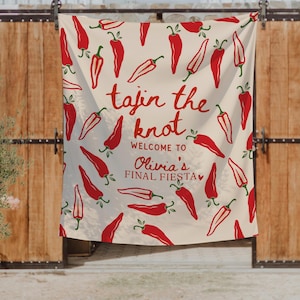 May include: A cream-colored fabric banner featuring a repeating pattern of red chili peppers. The text reads: tajin the knot, WELCOME TO, Olivia's FINAL FIESTA, with a small red heart icon. The design is printed in red and dark red ink.