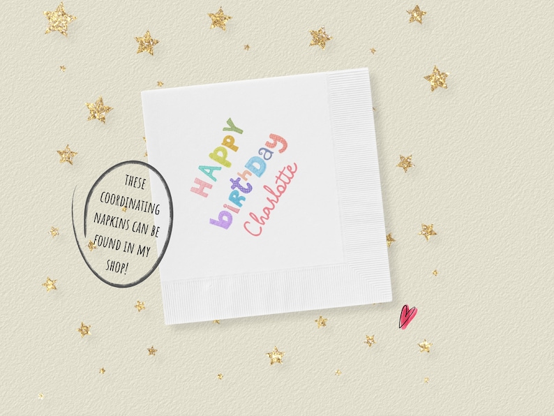 May include: A square white paper napkin featuring the text Happy Birthday Charlotte printed in a multi-colored, playful font. The napkin has a textured border and is surrounded by small gold glitter star shapes and a single small pink heart icon.