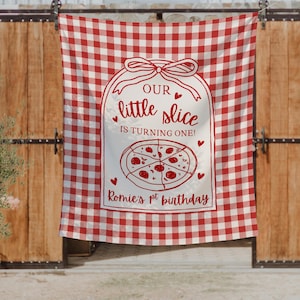 May include: A red and white gingham patterned fabric backdrop featuring a central white label graphic with a bow. The text reads: OUR little slice IS TURNING ONE! ROMIE'S 1st birthday, accompanied by a pizza illustration and small red hearts.