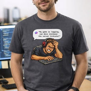 Könnte beinhalten: Dunkelgraues T-Shirt mit einem Grafikdesign eines frustrierten Gamers mit roten Kopfhörern, einer Tastatur und einer Sprechblase. Die Sprechblase sagt: "Mein Spiel ruckelt, können die Entwickler die Server-Tickrate erhöhen?"